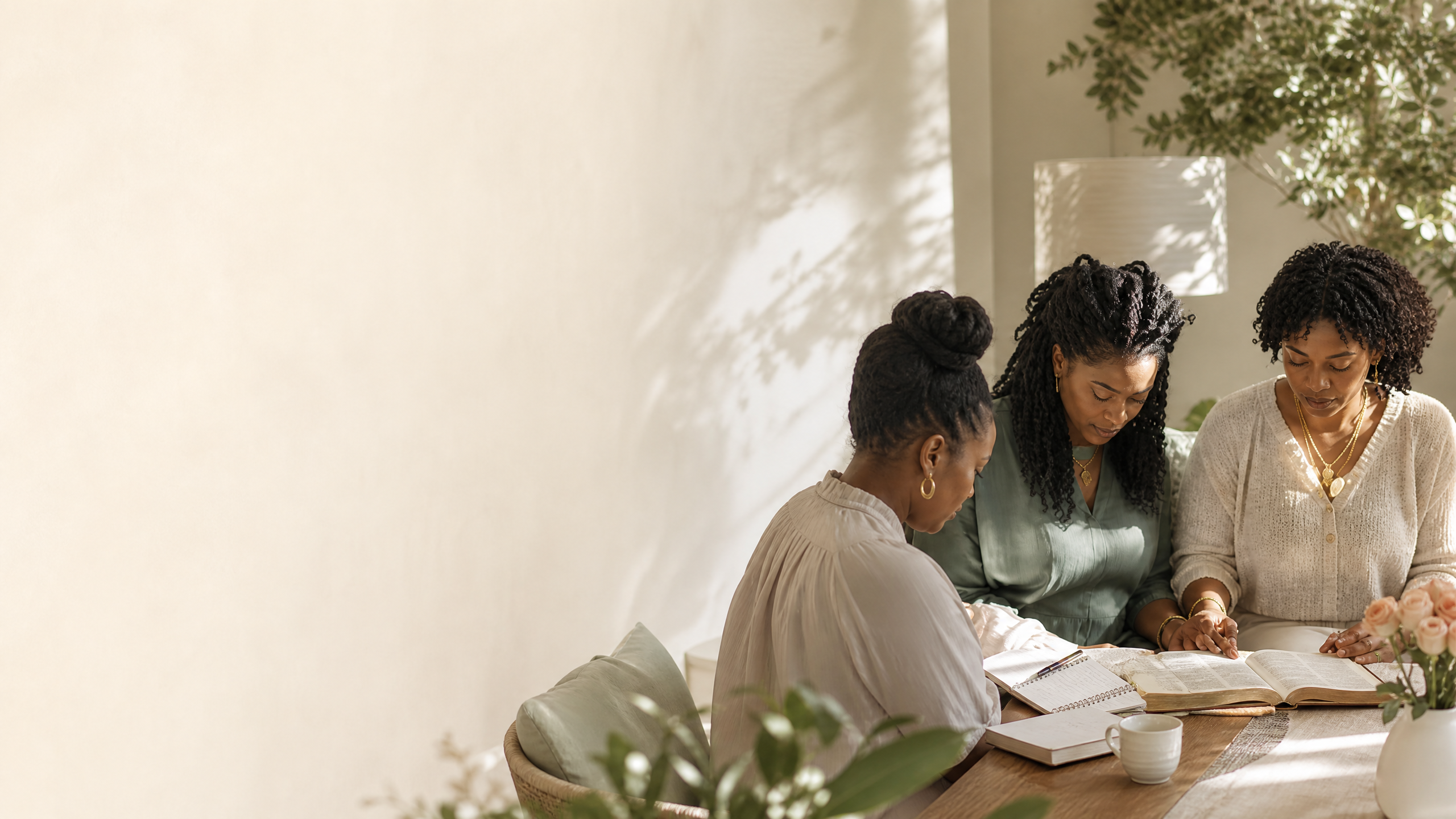 Young Black women gathered around an open Bible in prayer and fellowship
